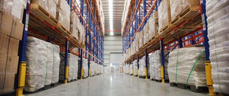 Clean, well-organized warehouse aisle with stacked pallets and tall shelving systems