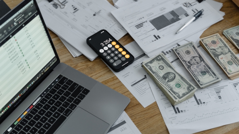 Laptop, calculator, cash, and financial charts on a desk showing how mathematics shapes effective financial strategies