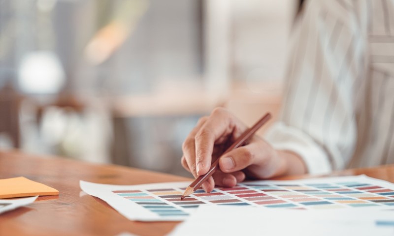 Close-up of a hand holding a pencil, pointing at a color swatch on a chart