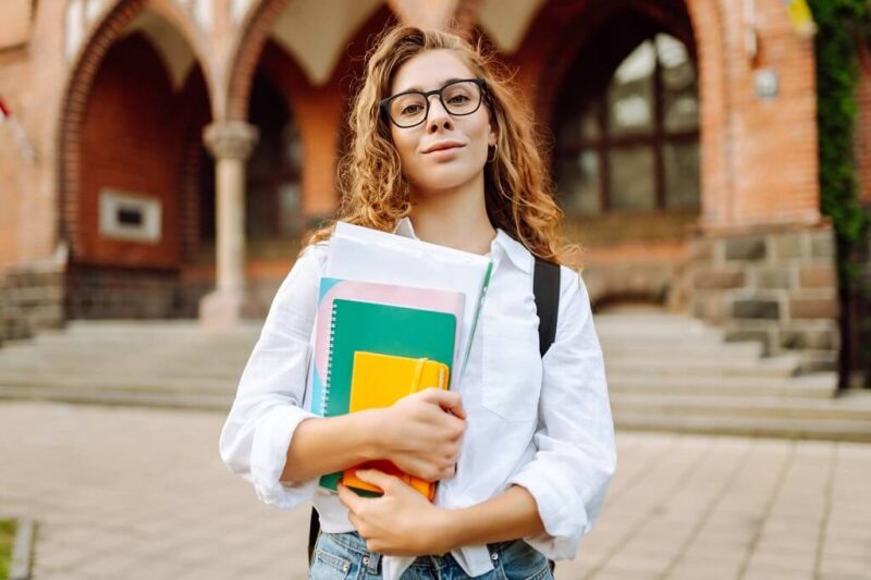 University student holding notebooks in front of a campus building