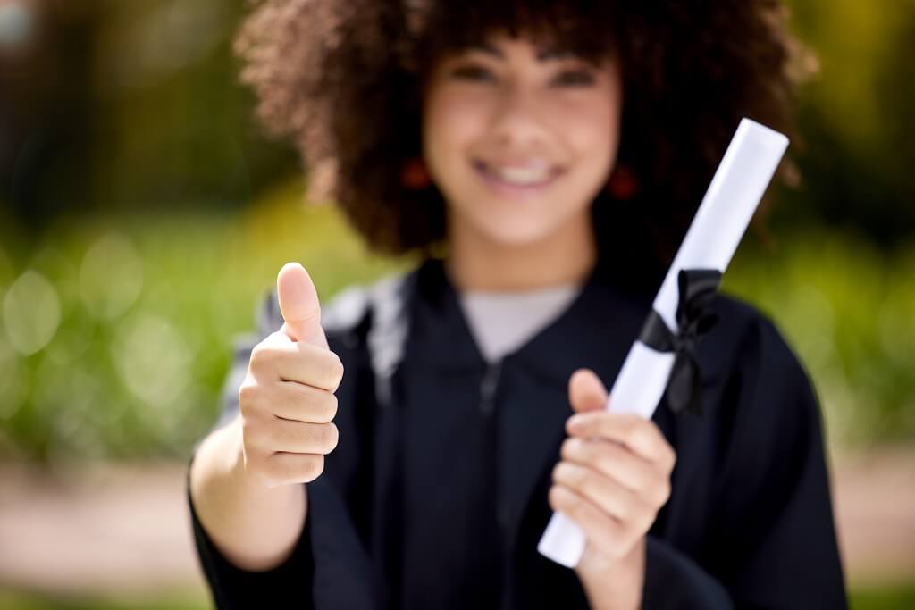 Graduate holding a diploma and giving a thumbs-up outdoors